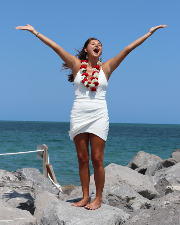 Sabrina, Certified Mental Performance Consultant, arms raised on a rocky shoreline